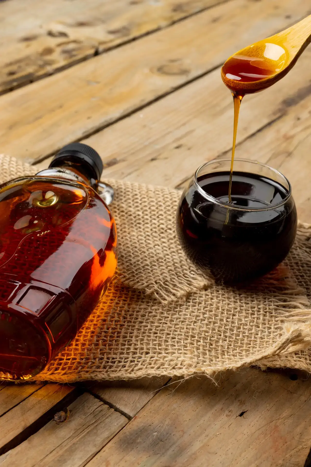 Horizontal image of bottle, wooden spoon and bowl of maple syrup on sackcloth and wood, copy space